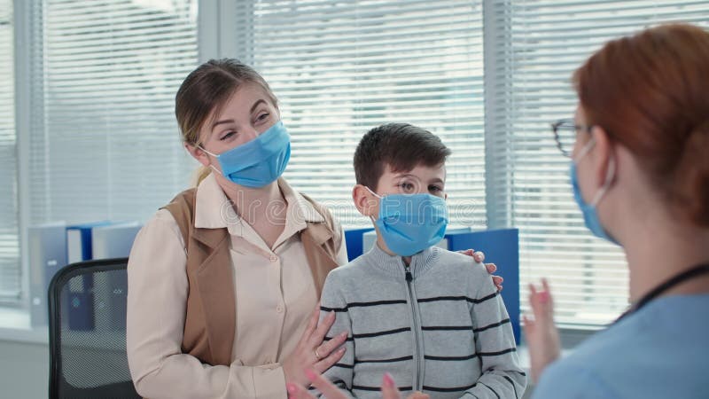 Segurança durante o retrato de quarentena de menino feliz com mãe em máscaras do médico do hospital mede temperatura