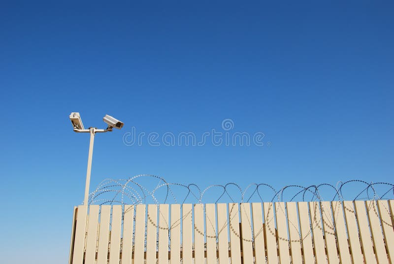 Fence with tracking cameras and barbed wire and on blue sky background. Fence with tracking cameras and barbed wire and on blue sky background