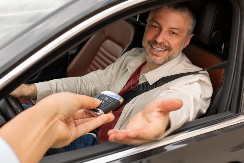 Sehenswerter Mann, der im Auto sitzt und den Schlüssel vom Mieter des Servicemitarbeiters oder Verkäufers abnimmt, der den Test du lizenzfreies stockbild