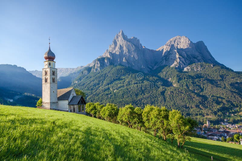 Panoramic view of idyllic mountain scenery in the Dolomites with St. Valentin Church and famous Mount Sciliar in beautiful morning light at sunrise, village of Seis am Schlern, South Tyrol, Italy. Panoramic view of idyllic mountain scenery in the Dolomites with St. Valentin Church and famous Mount Sciliar in beautiful morning light at sunrise, village of Seis am Schlern, South Tyrol, Italy