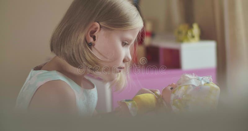 Seitenansicht der konzentrierten kleinen kaukasischen Mädchen, die mit Puppe spielt Schweres blondes Kind in elegantem Kleid stock video