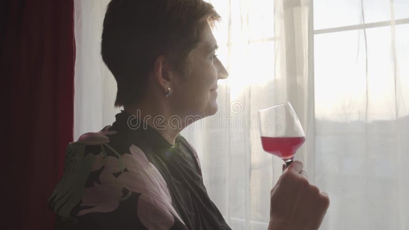 Seitenansicht der Senior Caucasian, die Weinglas hält und aus dem Fenster blickt Portrait der müden lächelnden Dame in