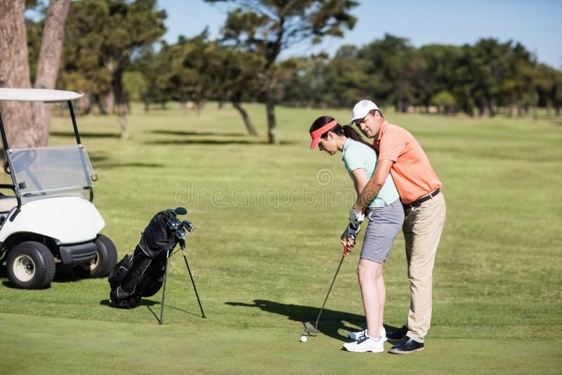 Seitenansicht der unterrichtenden Frau des Mannes, zum des Golfs zu spielen lizenzfreies stockbild Seitenansicht der unterrichtenden Frau des Mannes, zum des Golfs zu spielen lizenzfreies stockbild