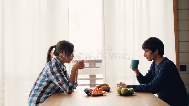 Seitenansicht des trinkenden Tees des Mannes und der Frau und Unterhaltungsin der Küche bei Tisch sitzen, die zusammen ruhigen Mo
