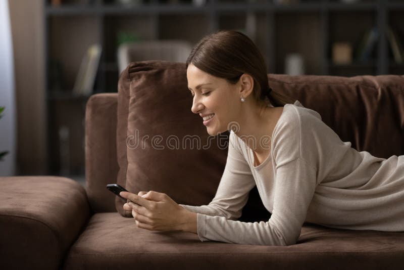 Seitenansicht lächelnde Frau mit Smartphone liegt auf einem gemütlichen Sofa lizenzfreies stockbild