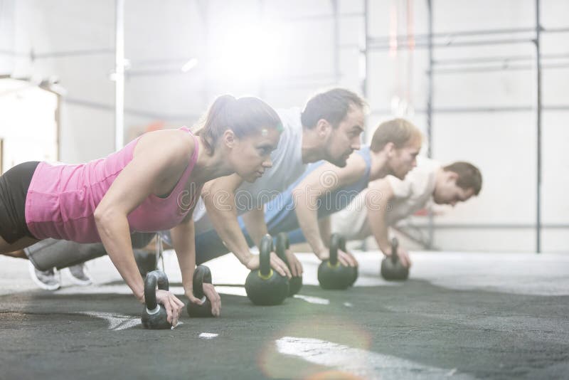 Seitenansicht von den entschlossenen Leuten, die Liegestütze mit kettlebells an crossfit Turnhalle tun lizenzfreie stockfotografie Seitenansicht von den entschlossenen Leuten, die Liegestütze mit kettlebells an crossfit Turnhalle tun lizenzfreie stockfotografie