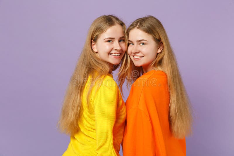 Seitenansicht von zwei lächelnden jungen blonden Zwillingsschwestermädchen in der klaren bunten Kleidung, welche die Kamera lokal stockfoto Seitenansicht von zwei lächelnden jungen blonden Zwillingsschwestermädchen in der klaren bunten Kleidung, welche die Kamera lokal stockfoto