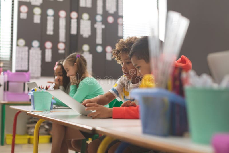 Seitenansicht von zwei Mischrasseschuljungen, die in der Schule ihr Notizbuch im Klassenzimmer betrachten lizenzfreies stockbild Seitenansicht von zwei Mischrasseschuljungen, die in der Schule ihr Notizbuch im Klassenzimmer betrachten lizenzfreies stockbild