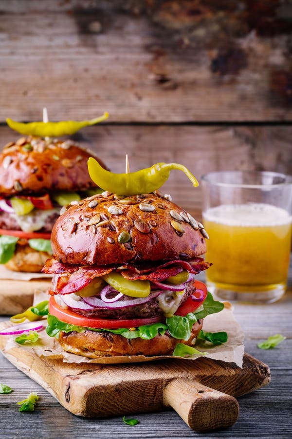 Selbst gemachte Burger mit ganzem Kornbrötchen, gebratenem Speck und würzigen in Essig eingelegten Pfeffern lizenzfreie stockfotografie