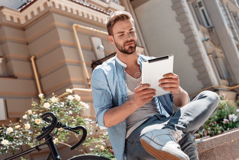Selbst-Glaube und harte Arbeit erwerben Ihnen Erfolg immer Junger lächelnder Mann, der im Park, seine Tablette halten sitzt seins lizenzfreies stockfoto Selbst-Glaube und harte Arbeit erwerben Ihnen Erfolg immer Junger lächelnder Mann, der im Park, seine Tablette halten sitzt seins lizenzfreies stockfoto