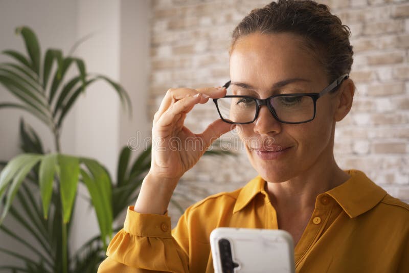Selbstbewusstes Porträt junger hübscher erwachsener Frauen, die zu Hause oder im Büro lächeln und Mobiltelefon benutzen. attraktiv lizenzfreie stockfotografie