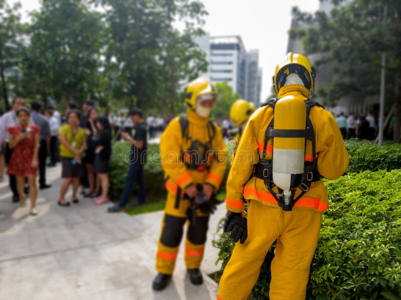 Select focus of back Firefighters in yellow suit with an oxygen tank in the back. Firefighters are teaching office workers to esca. Pe from high-rise buildings stock photo Select focus of back Firefighters in yellow suit with an oxygen tank in the back. Firefighters are teaching office workers to esca. Pe from high-rise buildings stock photo