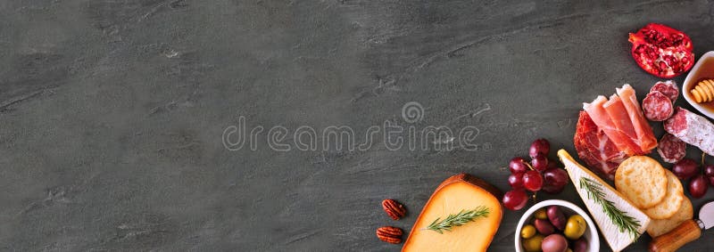 Selection of cheese and meat appetizers. Corner border banner, above view on a slate stone background with copy space