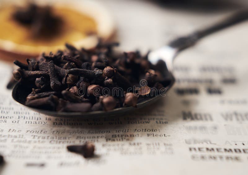 Selective focus on cloves in vintage spoon on vintage newspaper. Soft focus background with orange and star anise on the top. stock photography Selective focus on cloves in vintage spoon on vintage newspaper. Soft focus background with orange and star anise on the top. stock photography