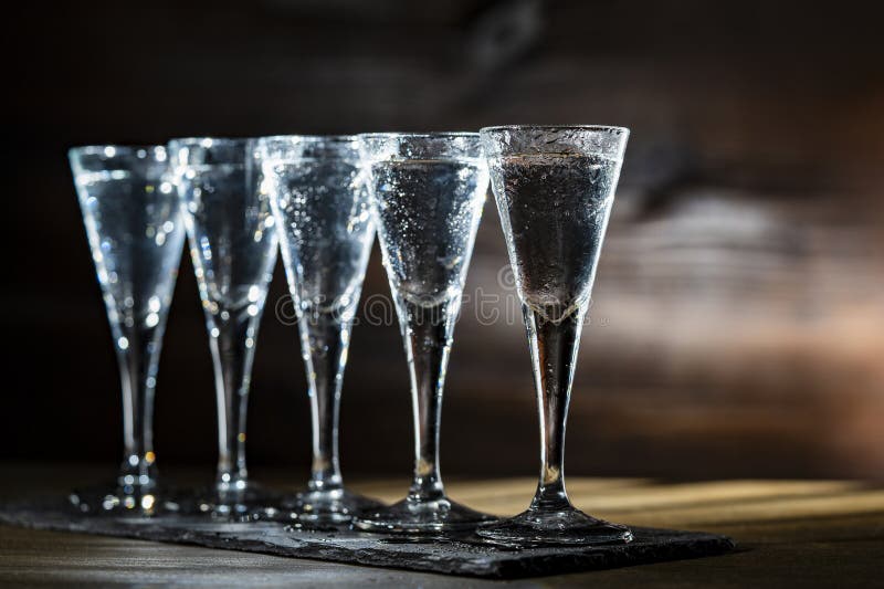 Selective focus of five shot glasses of cold vodka on wooden table, closeup stock photography