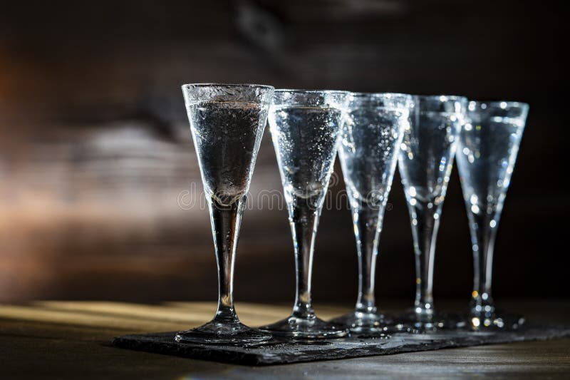 Selective focus of five shot glasses of cold vodka on wooden table, closeup stock photo