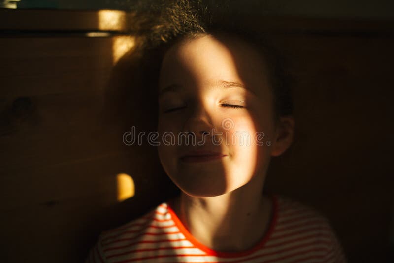 Selective focus. The little blonde cute girl smiles with closed eyes. Sunset warm light. Sunlight in hair. Summer happy time stock image Selective focus. The little blonde cute girl smiles with closed eyes. Sunset warm light. Sunlight in hair. Summer happy time stock image