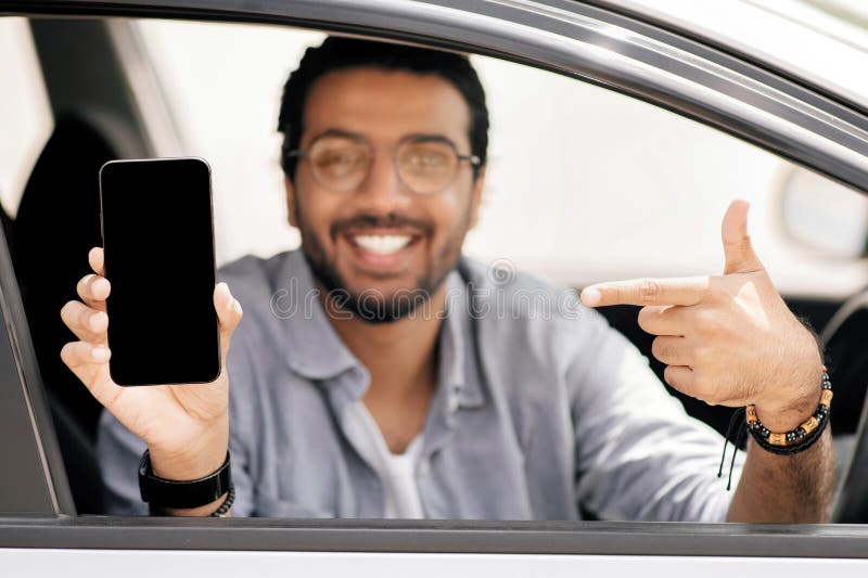 Selective focus on phone with empty display in guy hand. Selective focus on mobile phone with empty display in smiling middle-eastern guy hand, arab man driver using mobile application for navigation or car renting service, copy space, mockup