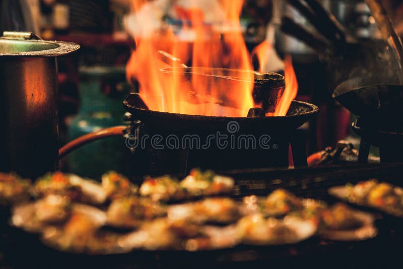 Grilled scallops sold at a street market stall with a pan covered with flames on the background. Chinatown, Bangkok, Thailand