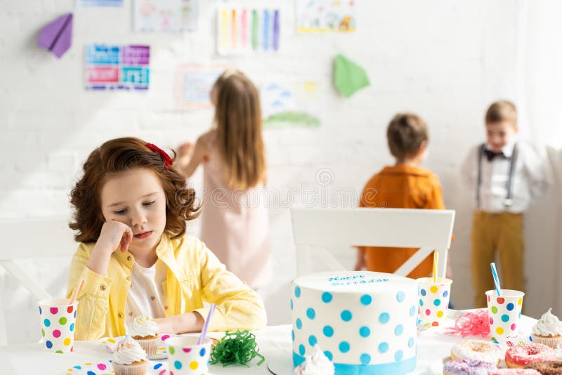 Selective Focus of Sad Kid Sitting at Table with Cake during Birthday