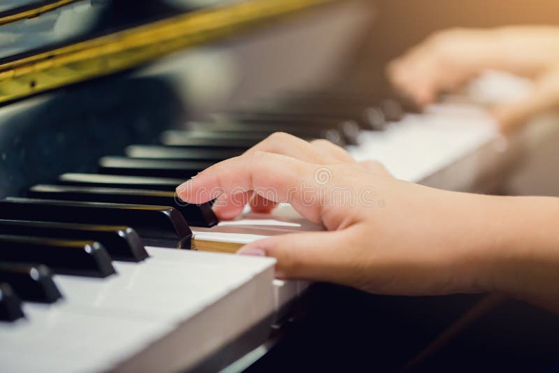 Selective focus to fingers of woman teaching boy to play the piano.