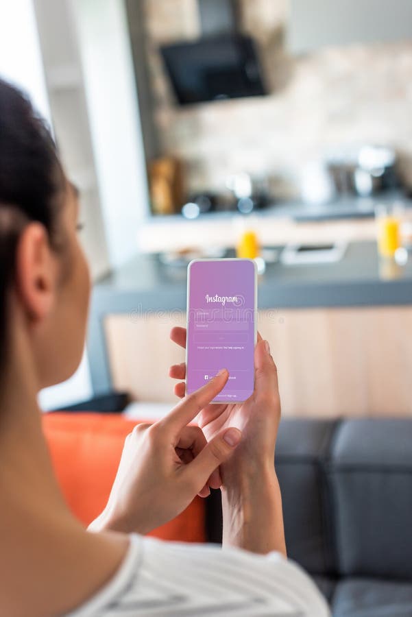 selective focus of woman using smartphone with instagram logo in kitchen