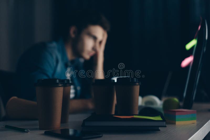 Selective focus of young programmer working at night near disposable cups. stock images