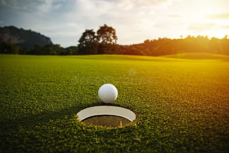 Selekcyjna ostrość białej piłki golfowej pobliska dziura na zielonej trawie dobry f