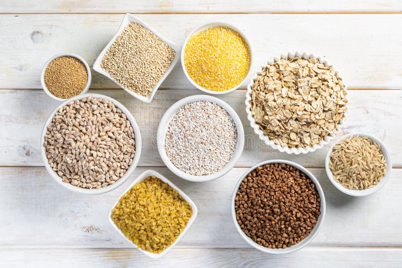 Selezione di interi grani in ciotole bianche - riso, avena, grano saraceno, bulgur, porridge, orzo, quinoa, amaranto