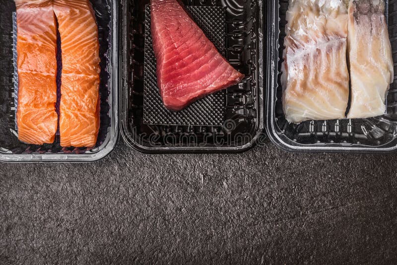 Seleção de faixas de peixes coloridas cruas: salmões, atum e bacalhaus em umas caixas plásticas no fundo rústico escuro, vista su fotografia de stock Seleção de faixas de peixes coloridas cruas: salmões, atum e bacalhaus em umas caixas plásticas no fundo rústico escuro, vista su fotografia de stock