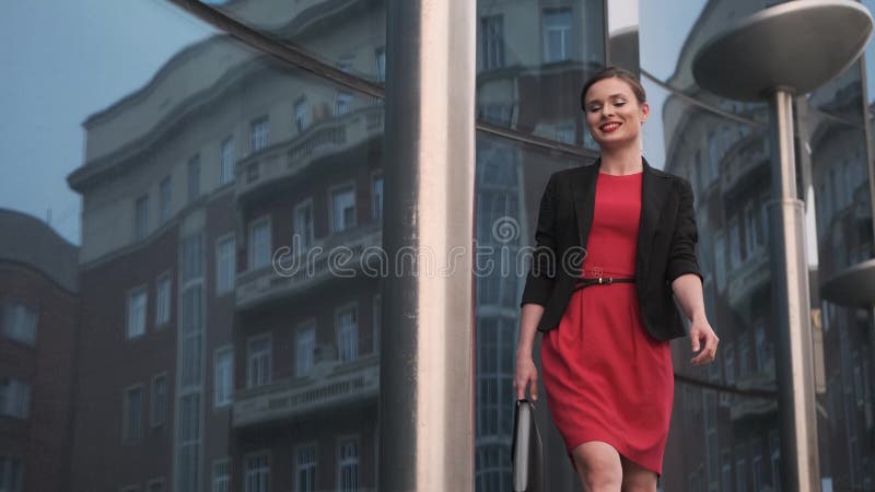 Self-confident business woman in a red dress walks against the backdrop of modern buildings. portrait of a young woman