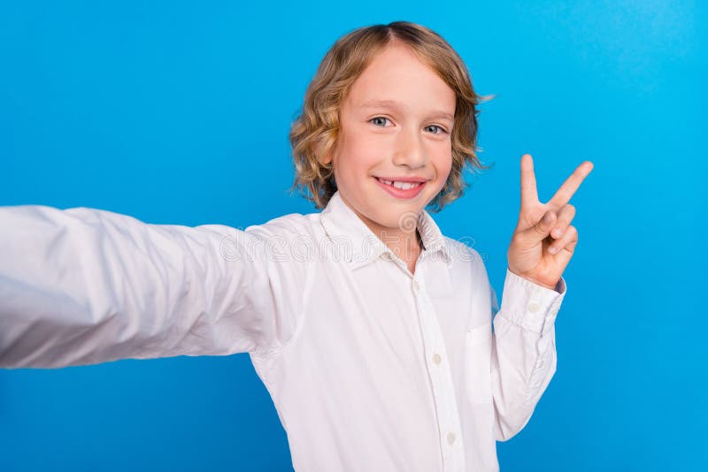 Self-portrait of handsome trendy cheerful boy showing v-sign good mood  over bright blue color background