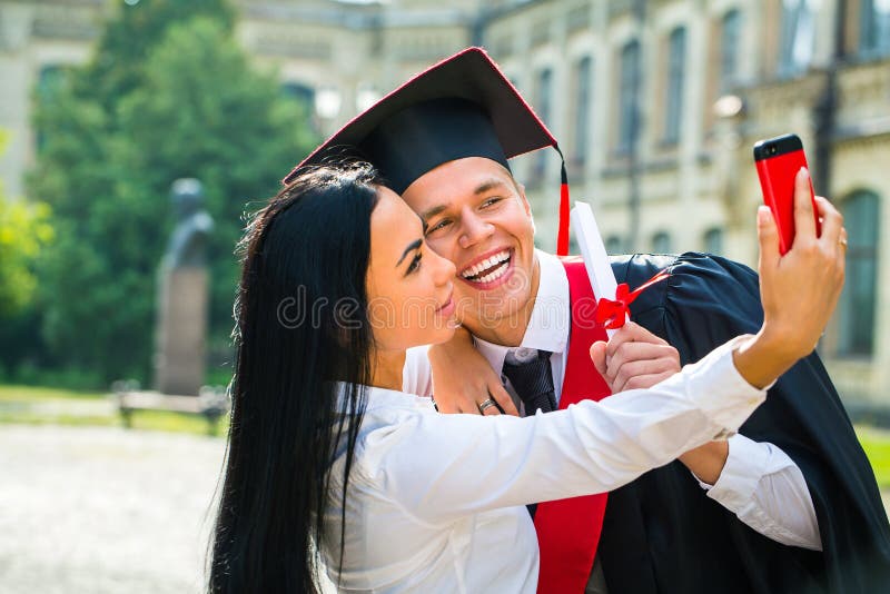 采取与外面手机的男性毕业生和女孩selfe 图库摄影