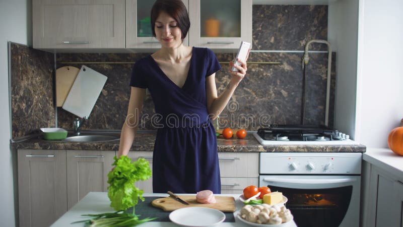 Selfie engraçado do tiro da dona de casa da mulher com telefone celular ao cozinhar na cozinha em casa dentro