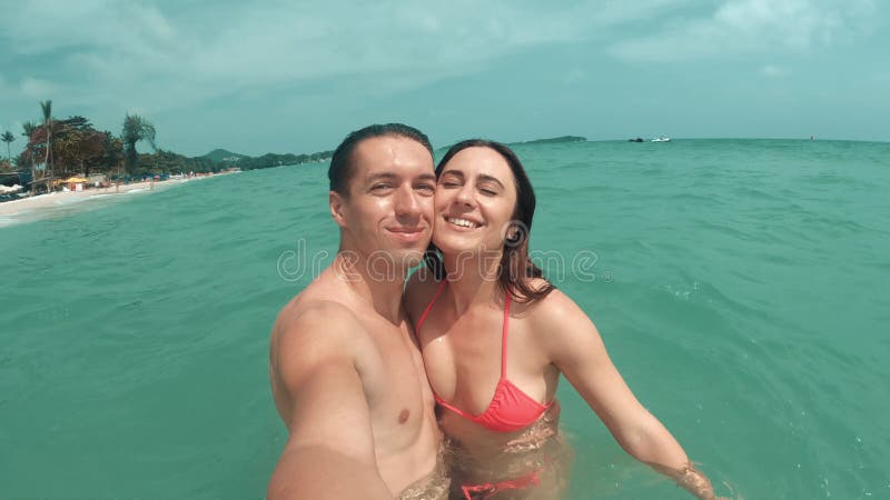 Selfie of loving couple in azure turquoise sea under bright sun. Happy couple enjoying romantic holiday at resort on hot