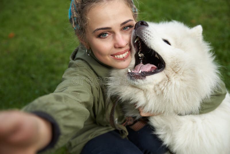 selfie of a young woman in green coat and multicolored dreadlocks with his white Samoyed dog in the autumn Park stock photo selfie of a young woman in green coat and multicolored dreadlocks with his white Samoyed dog in the autumn Park stock photo
