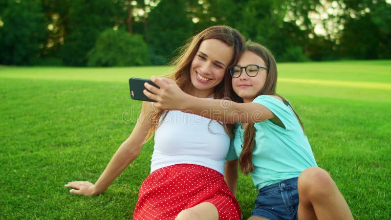 Selfie девушки и женщины на мобильном телефоне. Дочь и мать, сидя на траве акции видеоматериалы