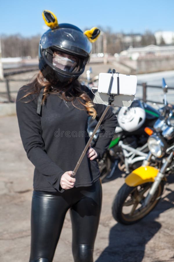 Selfies caucasianos novos da tomada do motociclista da mulher usando um telefone celular com monopod elástico imagens de stock Selfies caucasianos novos da tomada do motociclista da mulher usando um telefone celular com monopod elástico imagens de stock