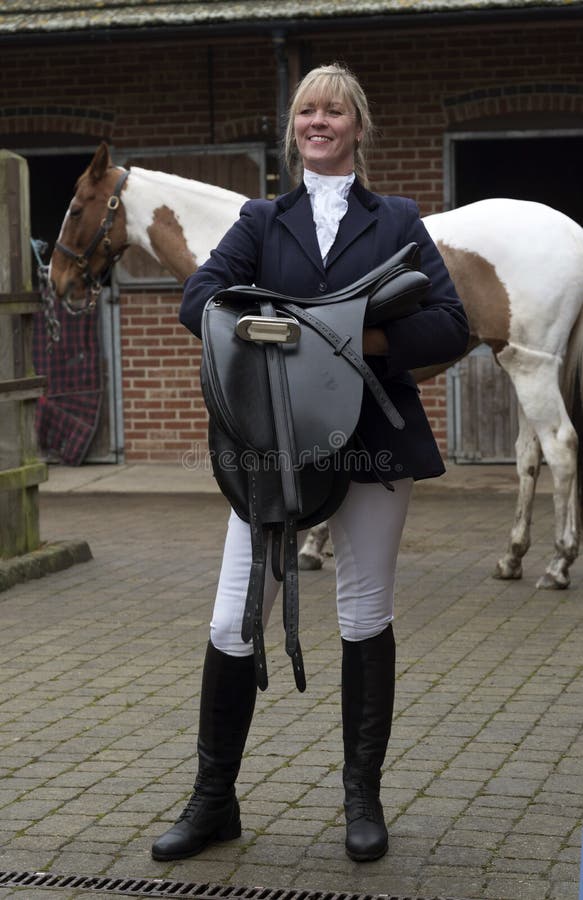 Sella della tenuta del cavaliere della donna con il suo cavallo fotografia stock Sella della tenuta del cavaliere della donna con il suo cavallo fotografia stock