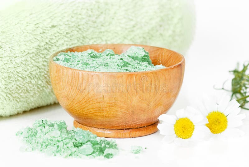 Green bath salts in a wooden bowl, a green towel and two camomiles. Green bath salts in a wooden bowl, a green towel and two camomiles