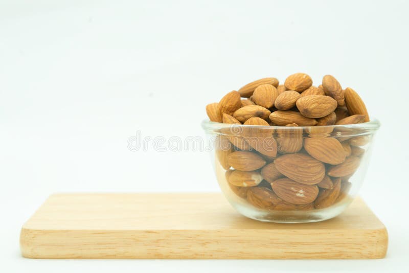 Semente da amêndoa do marrom da bacia de vidro na placa de madeira foto de stock