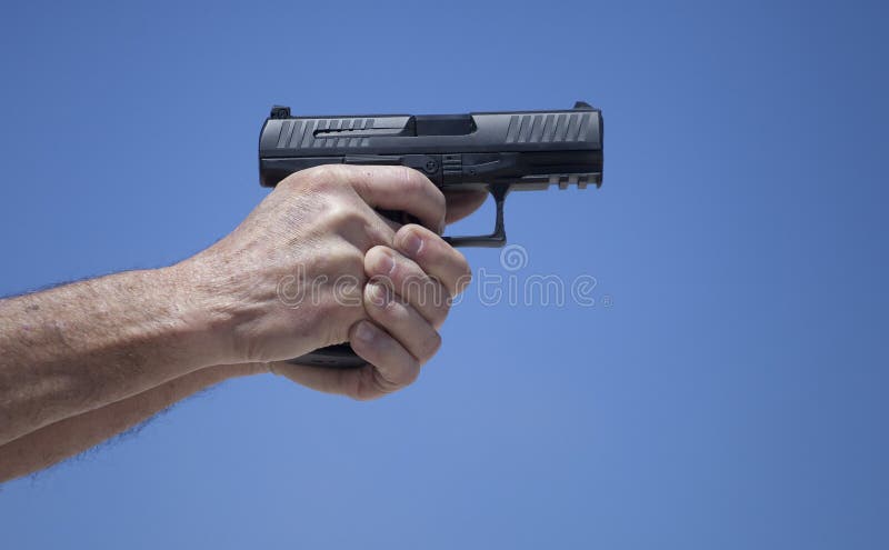 Black semi automatic handgun well gripped with sky behind. Black semi automatic handgun well gripped with sky behind