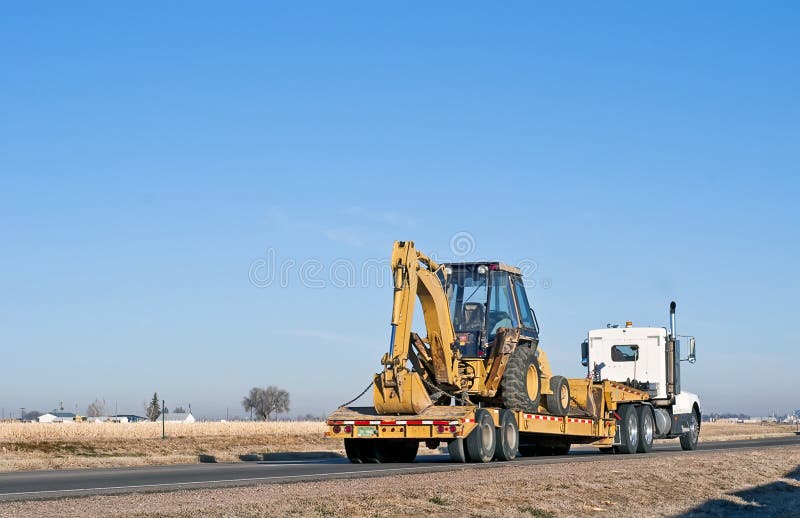 Big truck with a drop-deck trailer hauling a back-hoe tractor. Big truck with a drop-deck trailer hauling a back-hoe tractor.