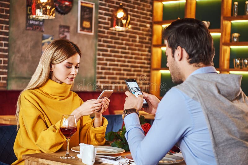 Sempre con lo smartphone Le giovani coppie stanno sedendo nel ristorante con gli smartphones fotografia stock libera da diritti Sempre con lo smartphone Le giovani coppie stanno sedendo nel ristorante con gli smartphones fotografia stock libera da diritti