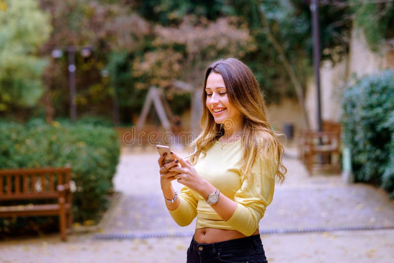 Senhora alegre que usa o smartphone no parque imagens de stock royalty free