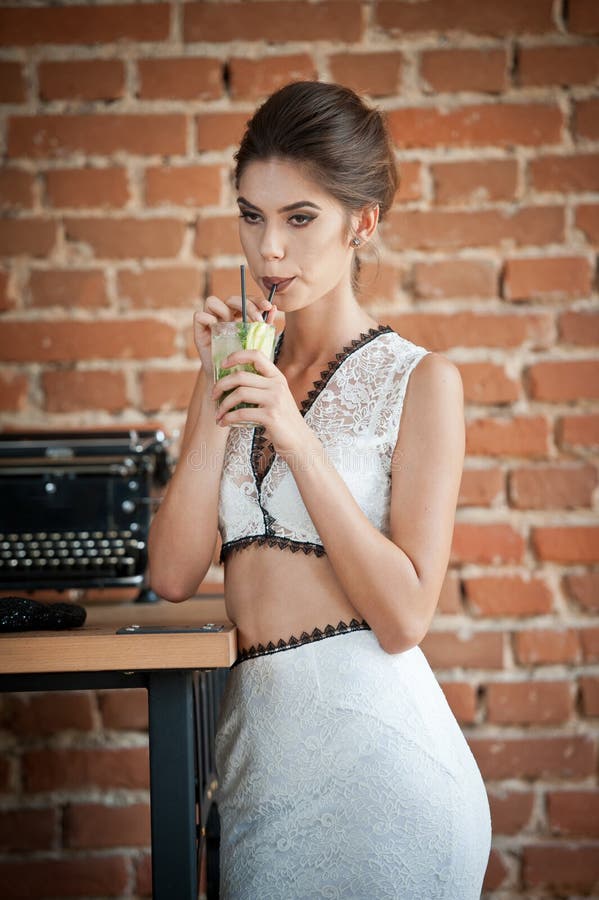 Senhora atrativa elegante com o vestido branco que está perto de uma tabela do restaurante que tem uma bebida Mulher do brunette imagens de stock royalty free Senhora atrativa elegante com o vestido branco que está perto de uma tabela do restaurante que tem uma bebida Mulher do brunette imagens de stock royalty free