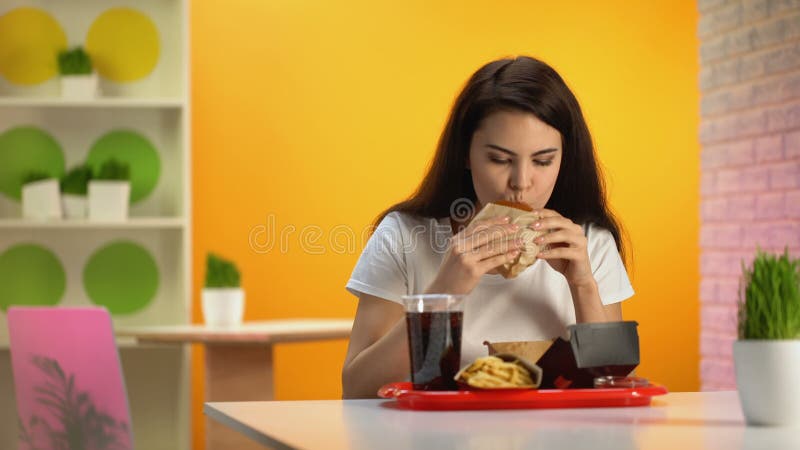 Senhora com fome que aprecia o gosto do Hamburger, jantar no restaurante do fast food, apetite