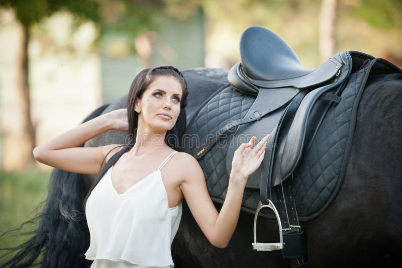 Senhora elegante com o vestido nupcial branco perto do cavalo marrom na natureza Jovem mulher bonita em um vestido longo que leva foto de stock Senhora elegante com o vestido nupcial branco perto do cavalo marrom na natureza Jovem mulher bonita em um vestido longo que leva foto de stock