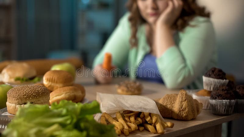 Senhora gorda deprimida que senta-se na tabela completamente da comida lixo insalubre, comendo demais