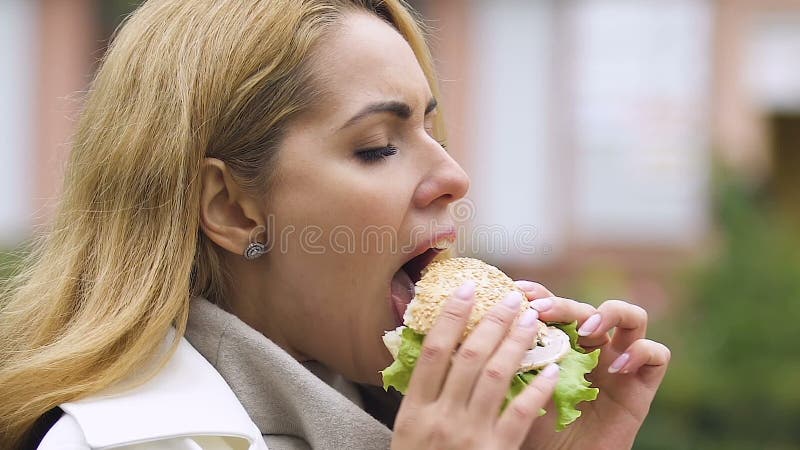 Senhora grávida com fome que come o hamburguer da carne, tendo o apetite saudável, hora do almoço